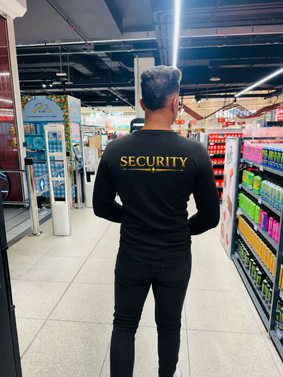 Operatore OnTopService di spalle, con maglia SECURITY, in presidio all’ingresso di un supermercato accanto alle barriere antitaccheggio